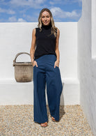 Model standing with hands in pocket wears high waisted, wide leg 100% cotton pants with highneck black rayon top