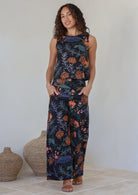 Model stands with both the hands in pocket wearing a 100% cotton wide leg pants in black based colorful botanical print