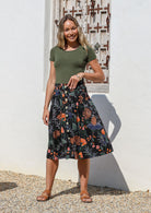 Woman wearing a basic green top and knee length button through cotton skirt with box pleats belt loops and pockets 