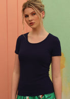 Woman wearing a scoop neck navy blue rayon fitted t-shirt in front of a green and pink wall.