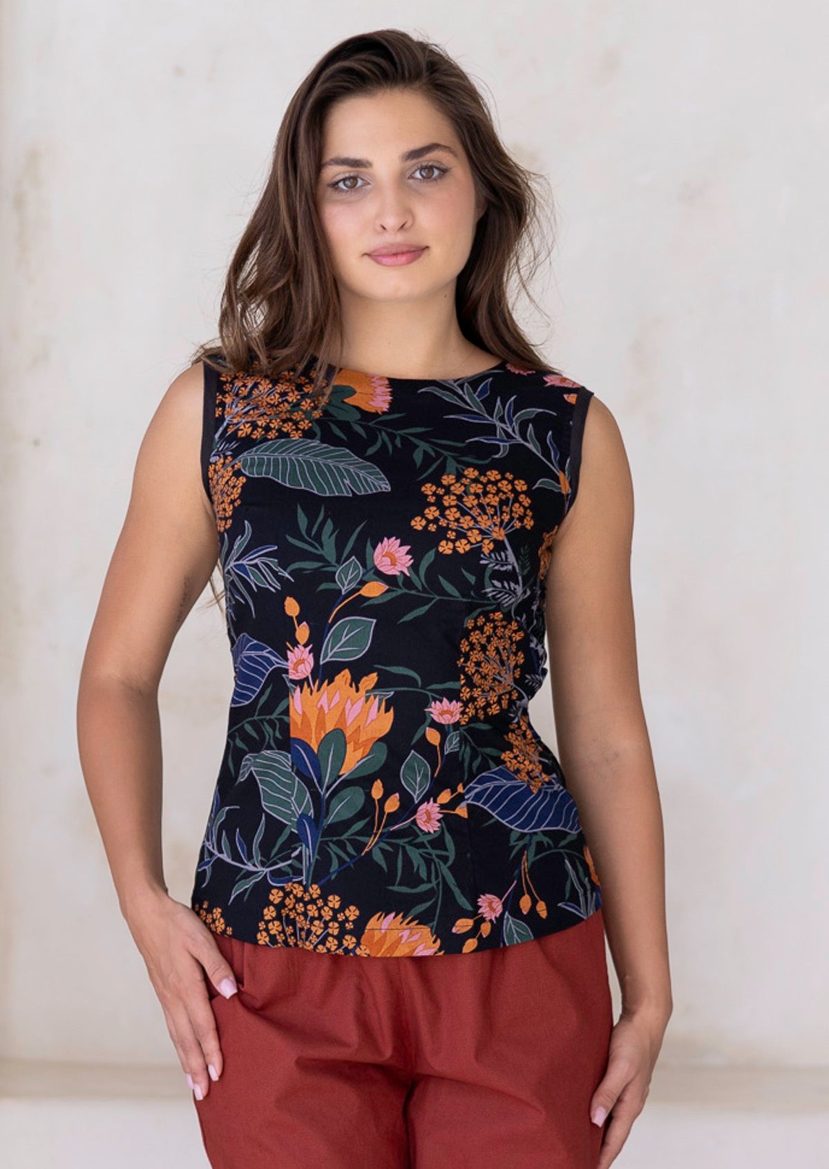 Woman wearing a black sleeveless top with floral pattern paired with rust coloured pants