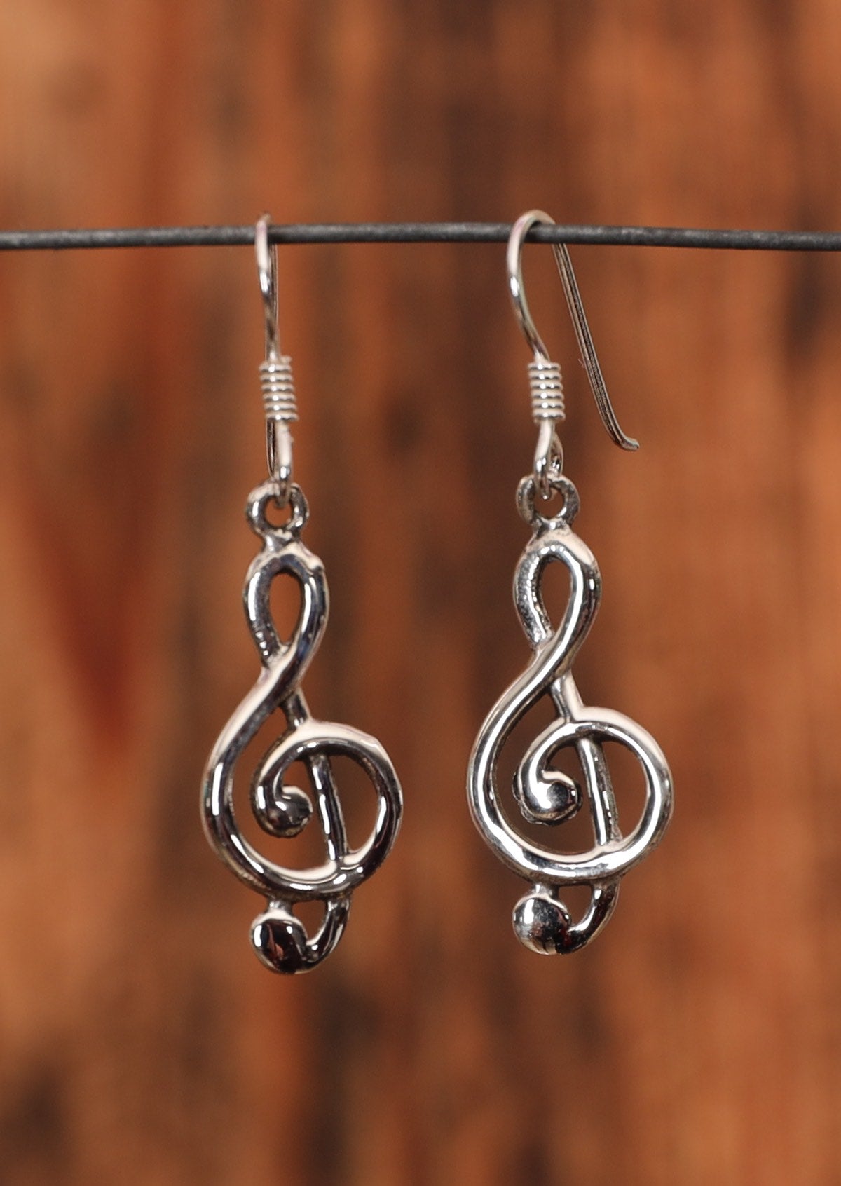 92.5% silver earrings in the shape of a treble clef on a wire for display.