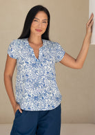 woman wearing a white based blue floral print cotton top against a white background.