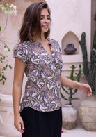 Woman in a printed cotton top and black pants standing in an outdoor setting with decorative pots and plants.