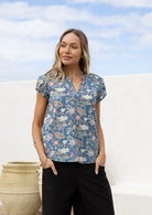 Woman wearing a cotton dusty blue floral print short sleeve blouse with V-neckline and elastic ruching at the front of the shoulders