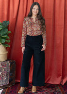 Woman wears cotton long sleeve top tucked in black corduroy pants.