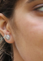Close-up of an ear wearing a silver sun and moon shaped studs with subtle carved faces