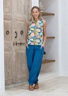 Woman wearing a pastel coloured sleeveless top and blue pants standing in a room with wooden doors.