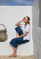 Model is sitting in dark blue 3/4 length wide-leg cotton pants with a wide waistband, side zipper, and pockets