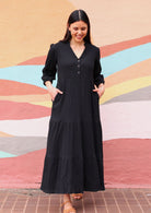 Woman wearing cotton gauze black maxi dress with pockets in front of mural