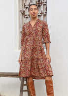 Woman wears cotton tiered dress in bright orangey red based floral print, with 3/4 sleeves, buttoned bodice and V-neckline