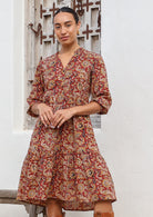 Woman poses in cotton tiered over the knee dress with 3/4 sleeves, buttoned bodice and V-neckline