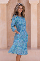 Woman wearing a aqua blue floral cotton dress with sleeves and lining, hands in pockets