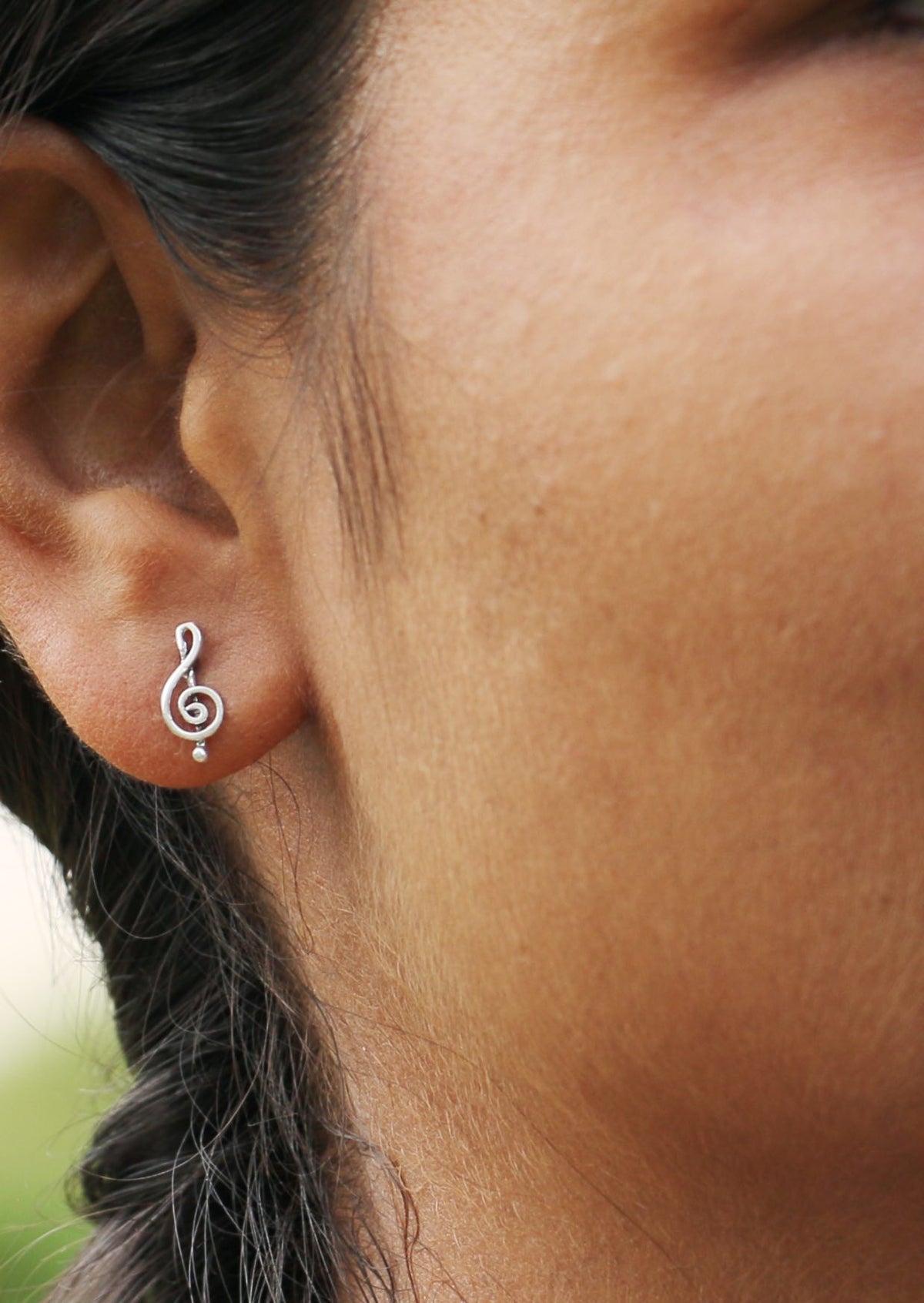 Close up of a woman wearing sterling silver Treble Clef studs featuring simple music inspired design