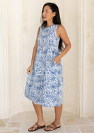 woman wearing a white based blue floral print, 100% cotton dress with her hand in pocket.