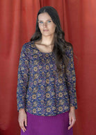 Woman wearing a 100% cotton long sleeved top in pink, cream and brown floral print on dark purple base.