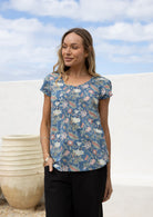 Woman wearing a blue floral short sleeve top with scoop round neckline and pleated detail across the bodice
