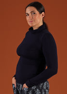 Side view of woman wearing a turtle neck navy blue fitted long sleeve soft stretch rayon top.