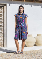 Woman wearing a cotton knee length day dress with a buttoned bodice, collar and cap sleeves