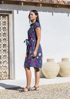 Woman wearing an abstract print cotton knee length dress with cap sleeves and a waist tie standing outdoors