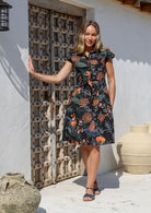 Woman wearing a black cotton floral dress with protea print and pockets 