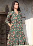 Model standing in sunshine wears a beautiful green cotton maxi dress with pockets, mandarin collar and 3/4 sleeves.