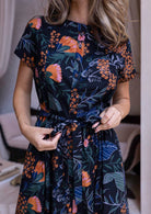 Model holds the fabric waist tie on a 1950's inspired beautiful botanical print dress with buttons in the centre front.