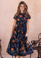 Model flaunting a retro style botanical print dress with detachable waist tie, pleats at the waist and hidden side pockets.