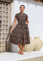 Woman wears 50's style cotton button through midi length dress with high round neckline, short sleeves and a waist tie.