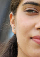 Close-up of a person wearing a sterling silver circular studs with cutout wave design and butterfly backs