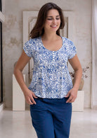Woman wearing a white based blue floral print cotton top with coconut buttons.