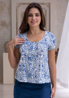 Woman wearing a white based blue floral print cotton top in an indoor setting.