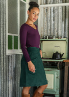 woman stands sideways wearing a cotton corduroy skirt and basic top standing indoors