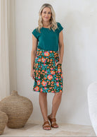 Woman stands in 100% cotton above knee length A-line skirt with piped detailing, pockets and a side zipper.