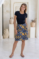Woman wears cotton A-line skirt in black based retro floral print with piped detail, paired with a black basic rayon top