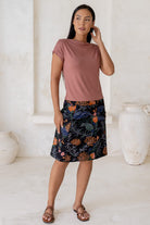 Woman wearing a dusty pink top and floral  cotton skirt in black with A-line shape, piped detailing and pockets.