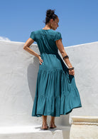 Back view of Woman in a teal dress standing against a white wall with blue sky.