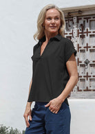 Woman stadning side on wearing a black cotton short-sleeve relaxed fit top with a collar and blue pants