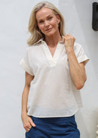 Woman wearing loose cut 100% cotton shirt style top with collar, V-neckline and folded cuff sleeves 