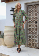 Woman wears cotton lightweight flowy maxi dress with pockets, mandarin collar and 3 tiered style in moss green based floral print