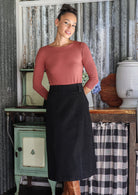 Woman in a rustic setting wearing a black cotton corduroy A-line midi length skirt and tan boots.