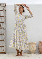 Woman poses in neutral based floral cotton maxi dress with buttoned bodice, 3/4 sleeves and flowy three tiered maxi skirt
