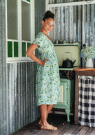 Woman in a cotton pale mint green based floral dress standing side on with hands in pockets