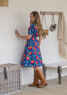 Model stands sideways wears 1950s inspired, button through shirt style dress with collar, short sleeves, waist tie and pockets.