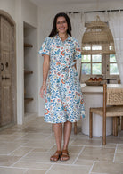 Woman wearing 100 percent cotton button through shirt dress with collar and short sleeves, in a white based floral print.