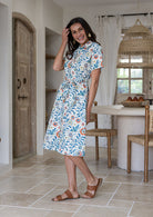 Model stands wears 1950s inspired, button through shirt style dress with collar, short sleeves, waist tie and pockets.