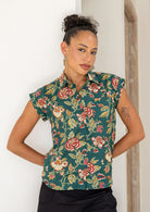 Woman wearing a 100% cotton green based floral top against a white wall