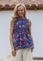 Woman wearing a 100% cotton blue floral sleeveless top with small pleated design, and buttoned mandarin collar.