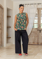 Woman posing in a minimalistic room wearing a cotton sleeveless top in green based floral print with small decorative pleats in the front.