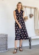 Woman wearing midi length, sleeveless  cotton dress with collar and pockets in black based floral print.